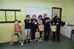 Zdjęcie kolorowe. W klasie umundurowane policjantki oraz dzieci stoją przy tablicy.