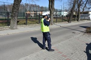 Umundurowany policjant stoi przy krawędzi jezdni i kontroluje prędkość pojazdów