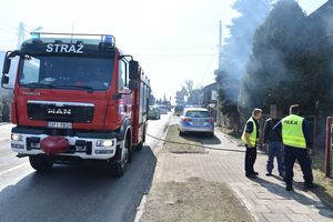 Strażacki wóz stoi na jezdni. W oddali widać policyjny radiowóz oraz policjantów wraz z mężczyzną