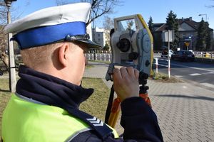 Umundurowany policjant obsługuje tachimetr na zdarzeniu drogowym