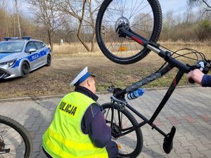 Umundurowany policjant sprawdzający rower. W oddali oznakowany radiowóz