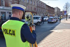 Umundurowany policjant obsługuje tachimetr na zdarzeniu drogowym