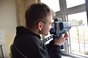 Uczeń stoi przy oknie i trzyma w ręku laserowy miernik prędkości
