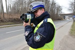 Umundurowany policjant drogówki kontroluje prędkość pojazdów przy pomocy laserowego miernika prędkości