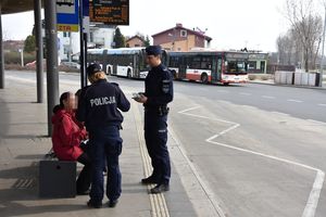 Umundurowani policjanci stoją na dworcu autobusowym i wręczają ulotki informacyjne