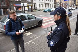 Umundurowana policjantka stoi na chodniku wraz z młodzieńcem, któremu wręczyła ulotkę informacyjną
