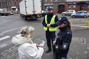 Umundurowani policjanci wręczają ulotkę informacyjna pieszej