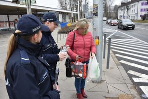 Umundurowani policjanci wręczają ulotki informacyjne pieszej przy oznakowanym przejściu dla pieszych