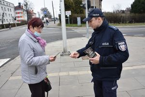 Umundurowany policjant wręcza ulotkę informacyjne pieszej przy oznakowanym przejściu dla pieszych