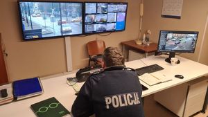 Umundurowany policjant siedzi za biurkiem i obserwuje zachowania uczestników ruchu drogowego na ekranach z kamer monitoringu miejskiego