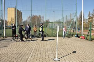 Miasteczko rowerowe. Umundurowany policjant w kamizelce odblaskowej stoi przodem do chłopca siedzącego na rowerze.