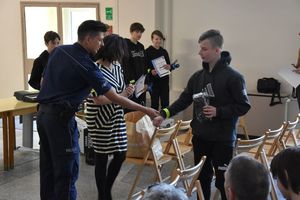 Umundurowany policjant wręcza opaskę odblaskową uczestnikowi turnieju