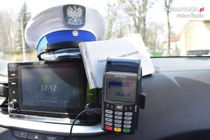 Terminal płatniczy zamontowany w radiowozie oraz czapka policjanta ruchu drogowego wraz z formularzami mandatu karnego