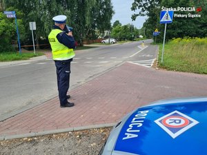 Umundurowany policjant ruchu drogowego kontroluje prędkość pojazdów w rejonie przejazdu dla rowerzystów