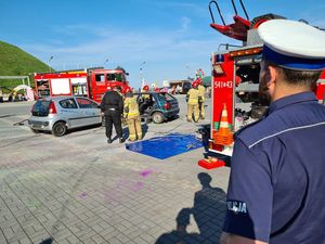 Zdjęcie kolorowe przedstawia policjanta oraz strażaków podczas pokazu ratownictwa drogowego