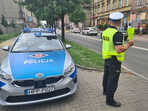 Umundurowany policjant stoi obok oznakowanego radiowozu.