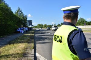 Policjant  ruchu drogowego stoi na drodze. W tle pielgrzymi