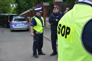 Funkcjonariusz ubrany w kamizelkę z napisem SOP. W tle policjanci