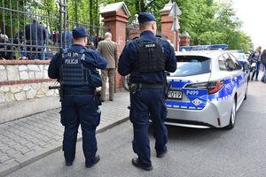 Policjanci stoją przy oznakowanym radiowozie