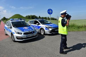 Umundurowany policjant kontrolujący prędkość pojazdów. W tle policyjne radiowozy