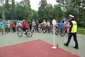 Policjant ruchu drogowego podczas egzaminu na kartę rowerową. W tle uczniowie z rowerami.