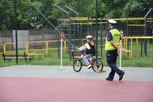 Policjant ruchu drogowego podczas egzaminu na kartę rowerową. Obok policjanta osoba egzaminowana jadąca na rowerze.