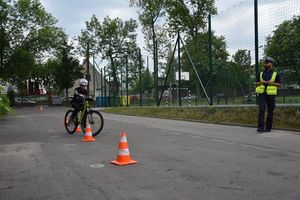 uczeń pokonuje tor przeszkód podczas egzaminu na kartę rowerową. Obok stoi policjant