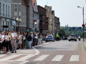 Ludzie idący w procesji. W oddali policjant oraz policyjny radiowóz zabezpieczający procesję