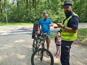 Policjant stoi obok rowerzysty, któremu wręcza odblaskową opaskę