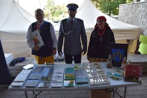 Policjant wraz z kobietą i mężczyzną stoją przy stole z regionalnymi artykułami.