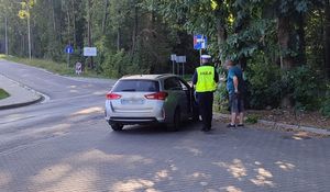 Policjant wraz z mężczyzną stoi obok kontrolowanego pojazdu