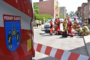 Zbliżenie na herb miasta Piekary Śląskie umieszczony na wozie strażackim. W tle miejsce wypadku drogowego