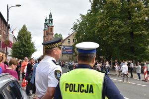 Policjant oraz strażnik miejski stoją przy radiowozie. W tle piekarska bazylika