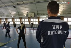 Osoby ćwiczące na sali gimnastycznej. Na pierwszym planie mężczyzna ubrany w bluzę z napisem KWP Katowice