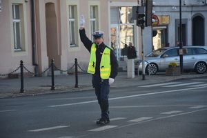 Policjant ruchu drogowego stoi na skrzyżowaniu z ręką uniesioną do góry