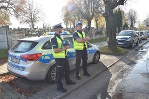 Umundurowani policjanci stoją obok radiowozu przy cmentarzu