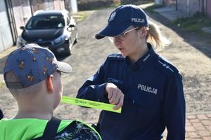Policjantka wręcza dziecku opaskę odblaskową