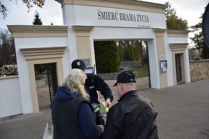 Policjant wręcza odblaski oraz ulotki przed bramą cmentarną