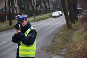 Policjant stoi przy drodze i kontroluje prędkość pojazdów