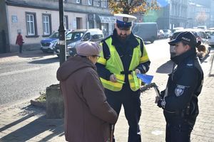 Policjanci wręczają odblask i ulotkę starszej kobiecie