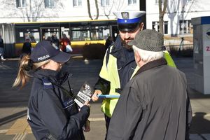 Policjanci wręczają odblask i ulotkę mężczyźnie na dworcu autobusowym