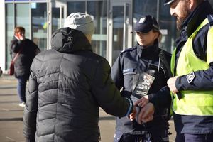 Policjanci wręczają odblask i ulotkę mężczyźnie na dworcu autobusowym