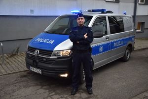 Policjant stoi przy oznakowanym radiowozie