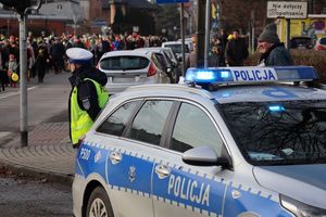 Zdjęcie przedstawia policjanta ruchu drogowego stojącego obok oznakowanego radiowozu podczas przemarszu Orszaku Trzech Króli.