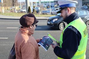 Zdjęcie przedstawia policjanta wręczającego odblask i ulotkę kobiecie