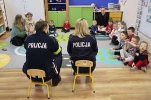Zdjęcie przedstawia policjantów siedzących na krzesełkach oraz grupę przedszkolaków siedzących na podłodze