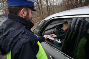 Zdjęcie przedstawia policjanta wręczającego ulotkę informacyjną oraz odblask kierującej samochodem osobowym