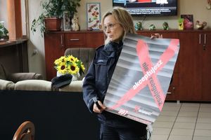 Zdjęcie przedstawia policjantkę, która trzyma w rękach plakat promujący kampanię społeczną nie reagujesz-akceptujesz