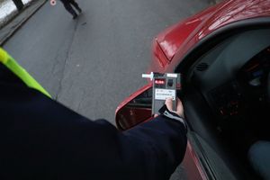 Zdjęcie przedstawia policjanta stojącego przy kontrolowanym pojeździe oraz trzymającego w ręce alkomat