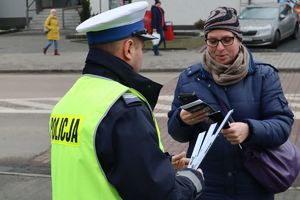 Zdjęcie przedstawia policjanta wręczającego odblask oraz ulotkę informacyjna kobiecie